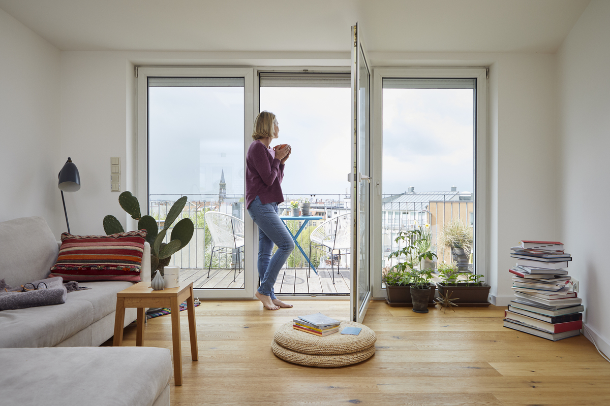 žena s hrnečkem kávy stojí mezi dveřmi na balkon a kochá se výhledem