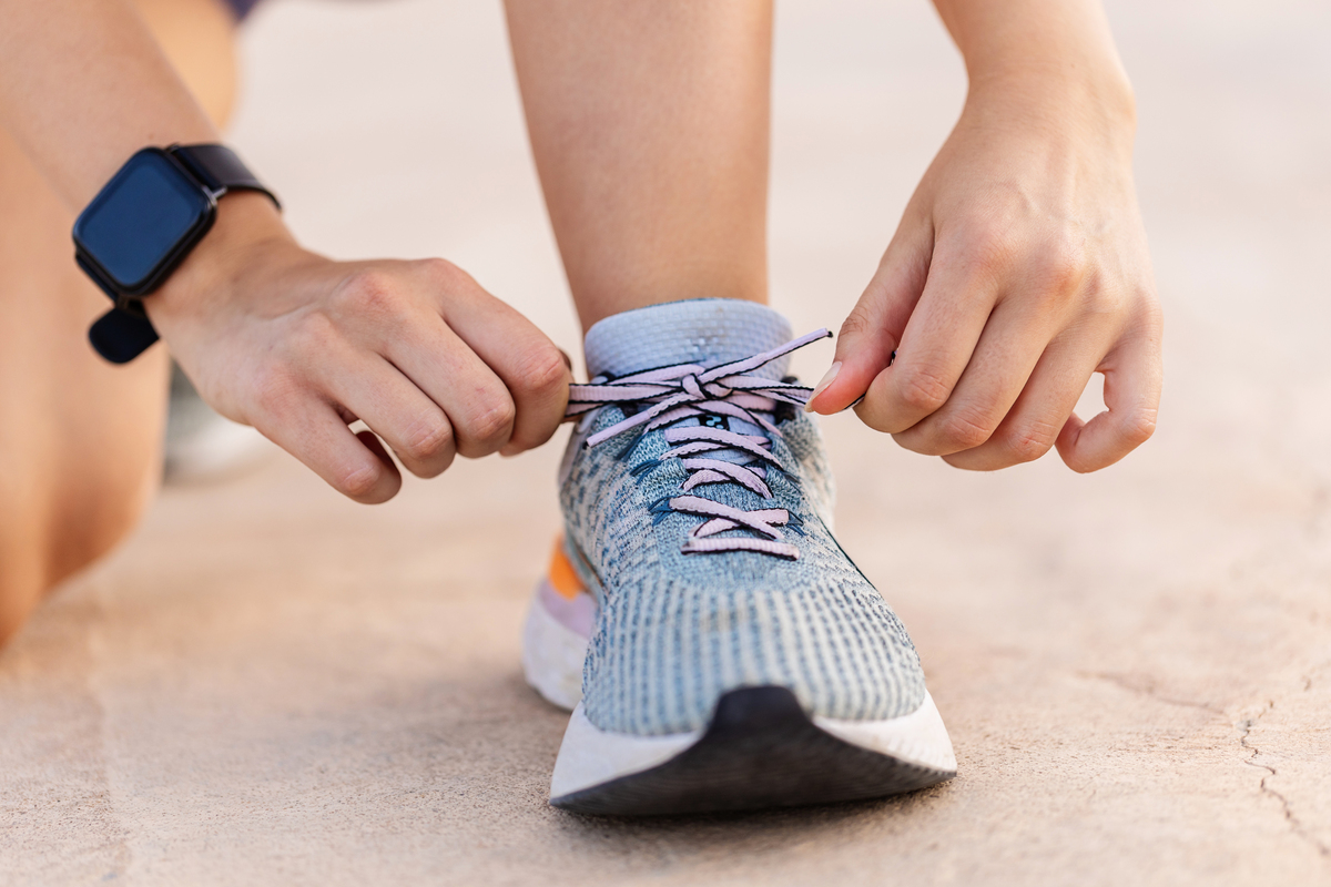Detailní záběr na ženskou běžkyni, která si zavazuje tkaničky u sportovních bot před zahájením běžeckého tréninku. Motivace, zdravý životní styl a fitness koncept.