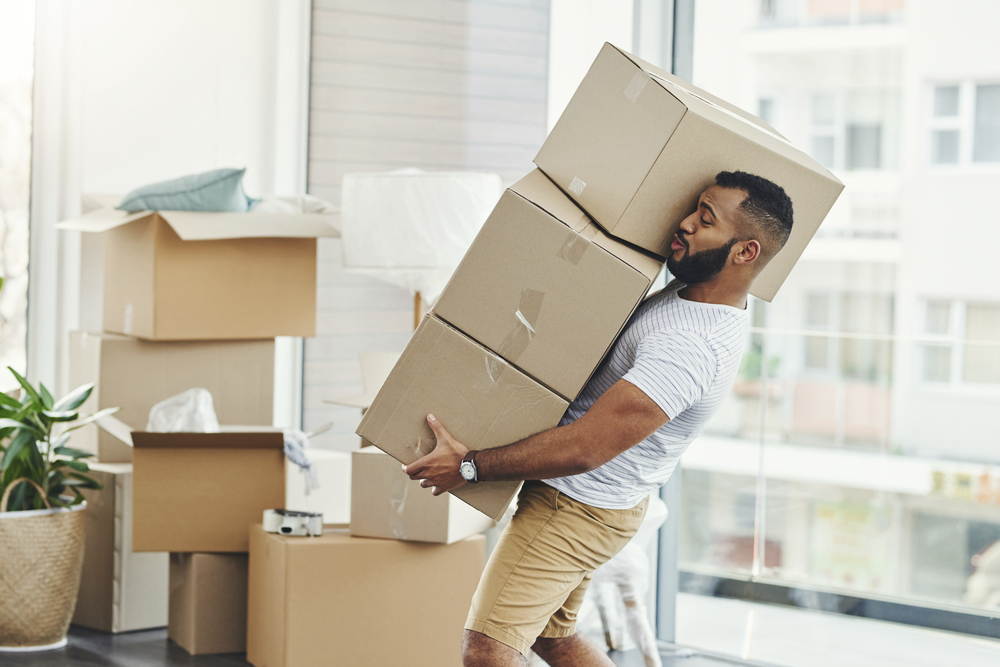 Mladý muž stěhující se do nového bytu nese několik krabic najednou
