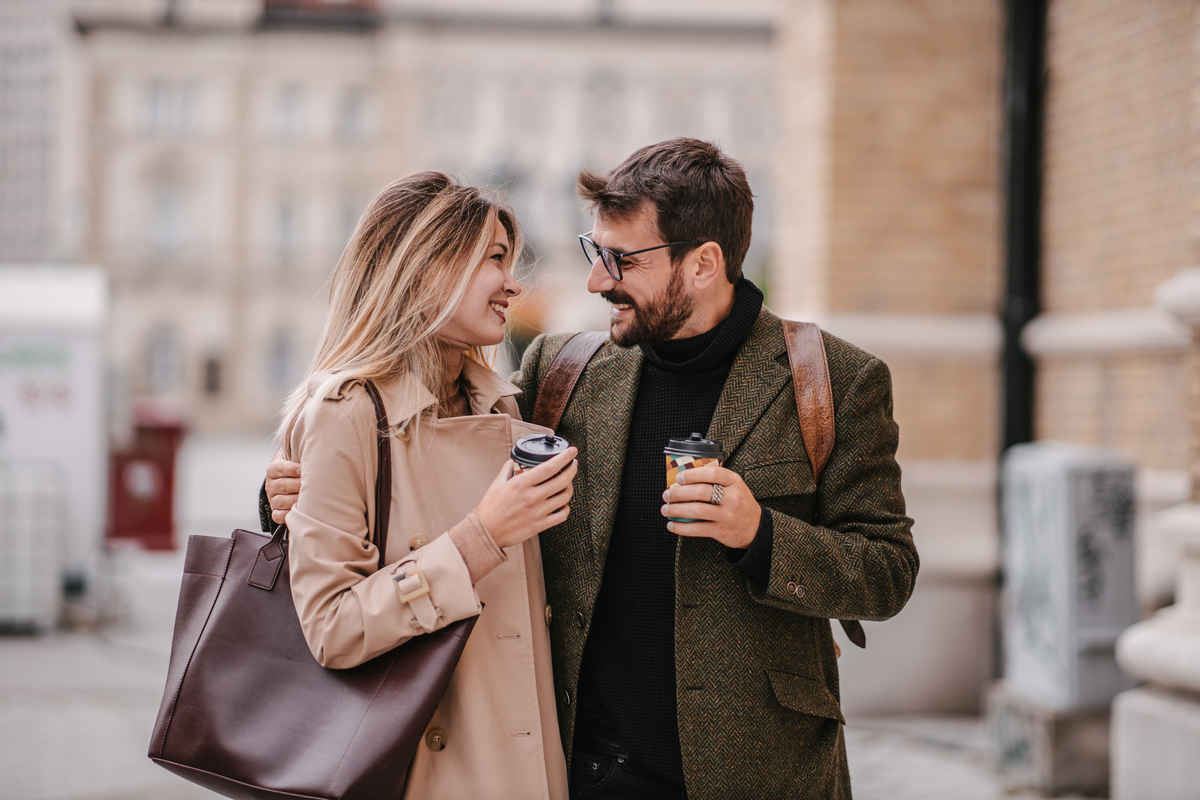 mladý pár si vykračuje městem s kávou v ruce a zamilovanými úsměvy na tvářích