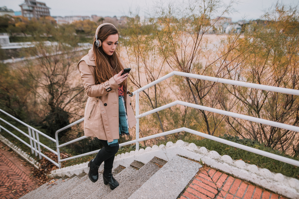 mladá žena se sluchátky a mobilním telefonem v ruce kráčí sama po schodech