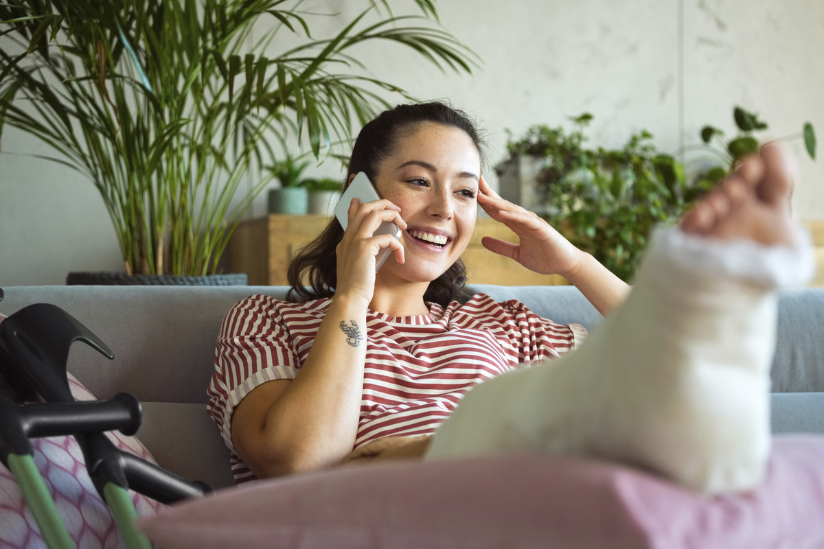 Mladá veselé žena se zlomenou nohou telefonuje