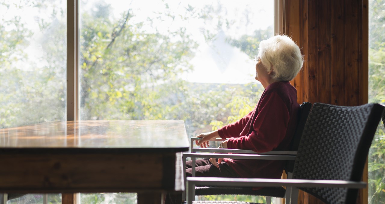 Zaopatřená starší dáma hledí oknem do zahrady.