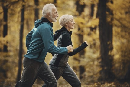 Pár aktivních pojištěných důchodců běží pro zdraví podzimním lesem